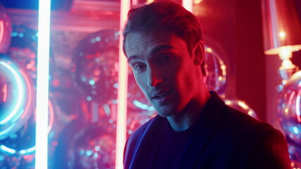 Affectionate guy smiling on neon lights background. Man winking at party