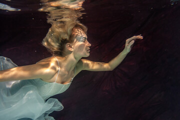 artistic woman wearing white wedding dress underwater
