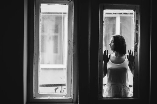 A beautiful girl standing on the windowsill in the white room