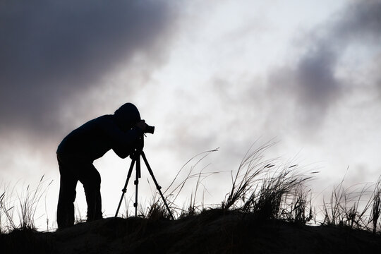 Silhouette of a photographer with a tripod against the sky with clouds