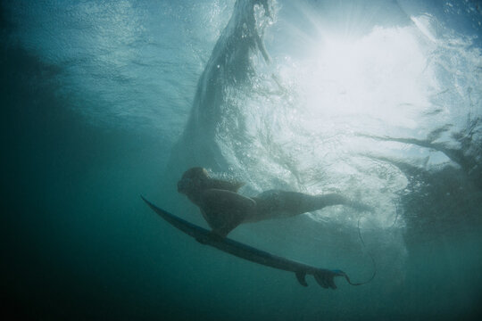 Girl surfer diving with a surfboard under the wave
