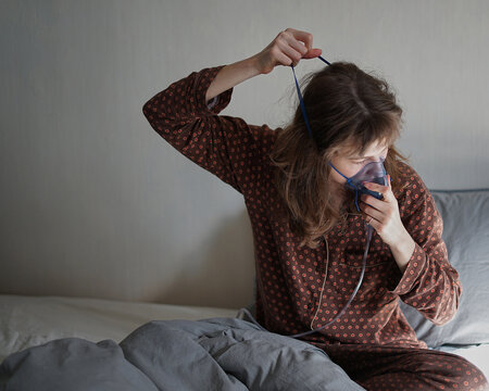 A sick woman at home alone in bed doing inhalation