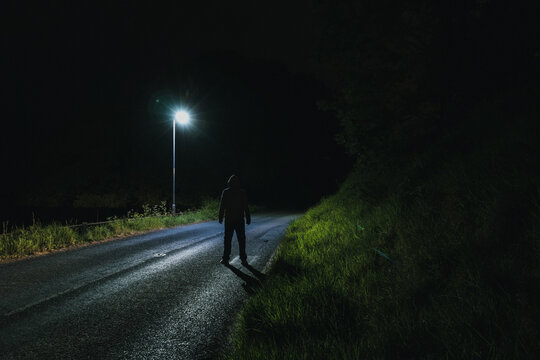 A sinister hooded figure, looking at a street light at night