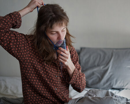 A sick woman at home alone in bed doing inhalation