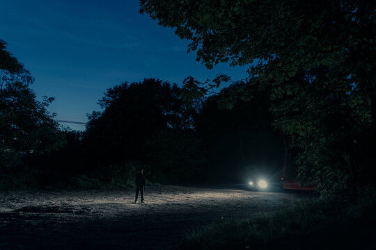 A Mysterious Figure Silhouetted Against Car Headlights At Night