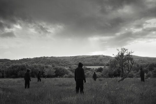Five spooky hooded figures, back to camera. Standing in a field.