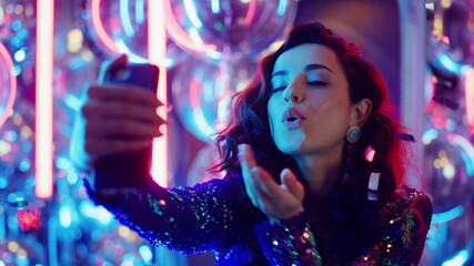 Brunette woman using smartphone on neon background. Girl making selfie at party