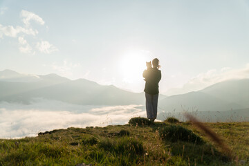 Woman standing with a dog on a meadow among mountains above clouds