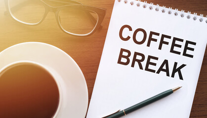 Coffee break - text on paper with a cup of coffee and glasses on a wooden background in sunlight.