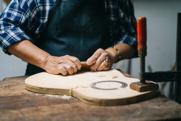 Luthier carving guitar wood while standing at workshop