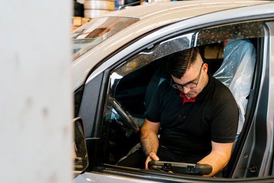 Mechanic examining car while sitting on vehicle seat in garage