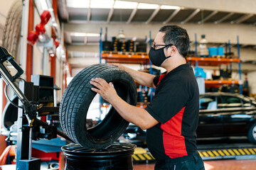 Mechanic wearing mask examining tire in auto repair shop