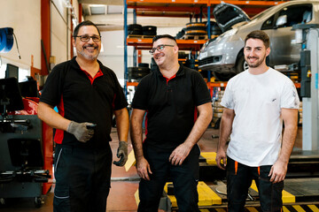 Smiling male coworkers standing in auto repair shop