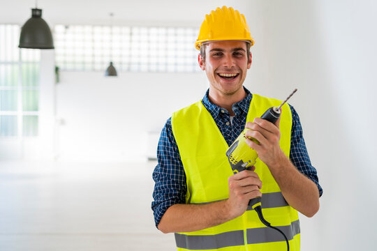 Smiling man holding drill machine while standing at office under construction