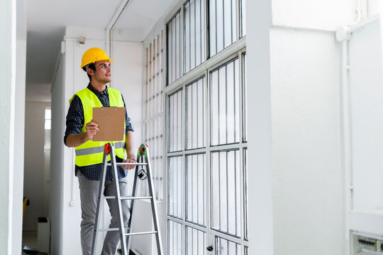 Man wearing work helmet and jacket standing on ladder by window at construction site