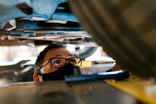 Close-up of mechanic wearing mask examining car in auto repair shop