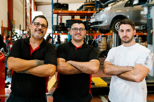 Confident male coworkers with arms crossed standing in auto repair shop