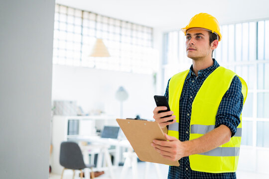 Architect holding notepad while using phone at construction site