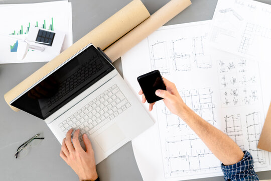 Architect using mobile phone while sitting by desk at office