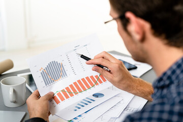 Man analyzing graph paper while sitting by desk at office