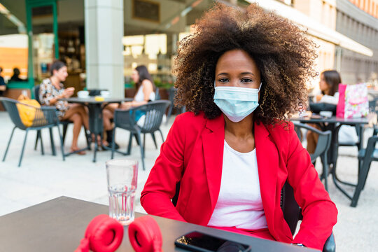 Woman wearing protective face mask sitting at sidewalk cafe