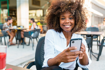 Woman text messaging on smart phone while sitting at cafe