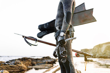 Man holding scuba mask and harpoon while standing at beach