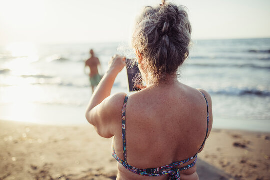 Woman taking photo through mobile phone while standing at beach
