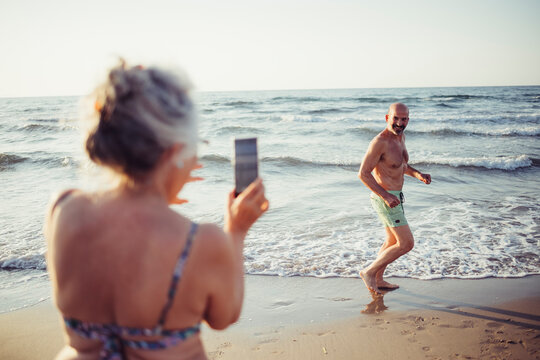 Woman taking photo of man running at beach