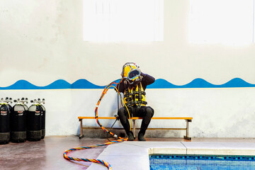 Man wearing diving suit while sitting on bench against wall at poolside