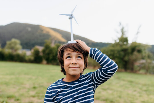 Smiling boy holding wind turbine toy on head while standing at backyard