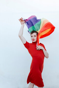 Non-Binary Person Waving Rainbow Flag While Standing Against White Background