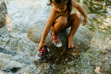 Cute girl playing in flowing water while sitting on rock during summer