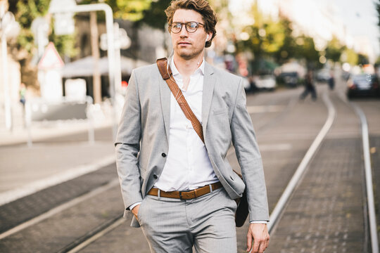 Handsome man with hands in pockets walking on tramway in city