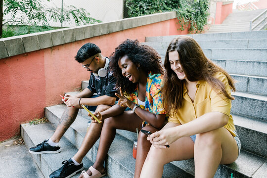 Young woman taking selfie while friends text messaging on smart phone sitting on steps