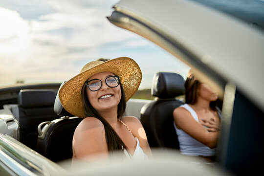 Young smiling woman traveling with friend in convertible car