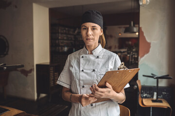 Portrait of chef with clipboard standing in restaurant