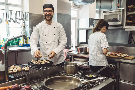 Portrait of smiling male chef cooking mushrooms in commercial kitchen