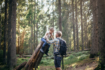 Father holding daughter over log in forest