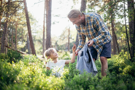 Smiling father looking at daughter collecting garbage in forest