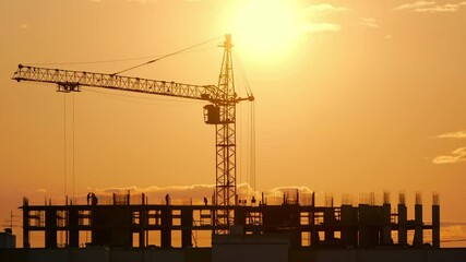 High tower crane in the center of the construction at sunset. The sun in the background