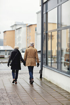 Rear view of senior couple holding hands while walking on sidewalk during winter