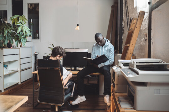 Computer programmers reading book for coding at workplace