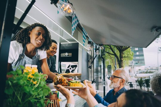 Smiling owners giving indian food to customers while standing in commercial land vehicle