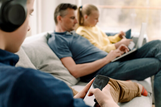 Teenager using smart phone while sitting on sofa with family