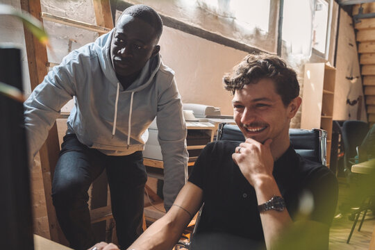 Smiling computer programmer by coworker working on coding at workplace