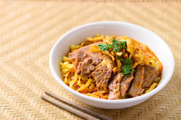 Northern Thai food (Khao Soi), Spicy curry noodles soup with beef in a bowl and chopsticks on woven bamboo background