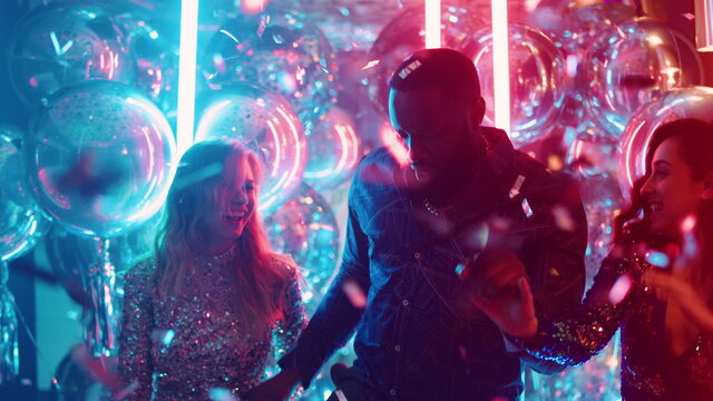 African guy and european girls dancing in nightclub. Friends having fun at party