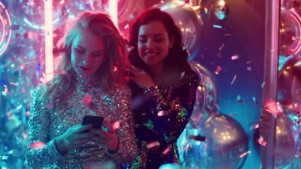 Beautiful girls looking at smartphone in club. Woman texting at party