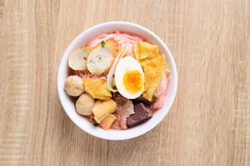 Thai food (Yen Ta Fo), Rice noodles soup with red sauce and fish tofu, pork ball and fried wonton in a bowl on wooden background, Top view